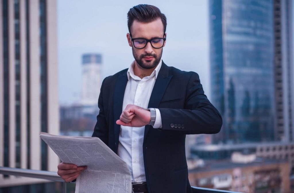 A man wearing stylish, oversized frames checks his watch.