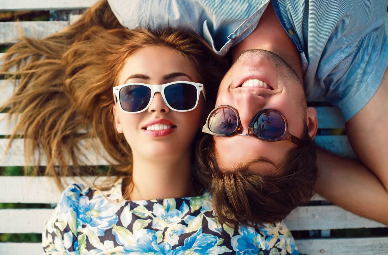 Young man and woman wearing sunglasses lying down outside on a deck.
