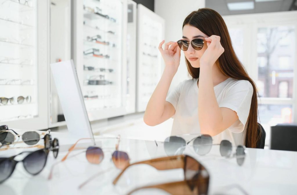Woman with long dark hair trying on sunglasses in an optometry shop.
