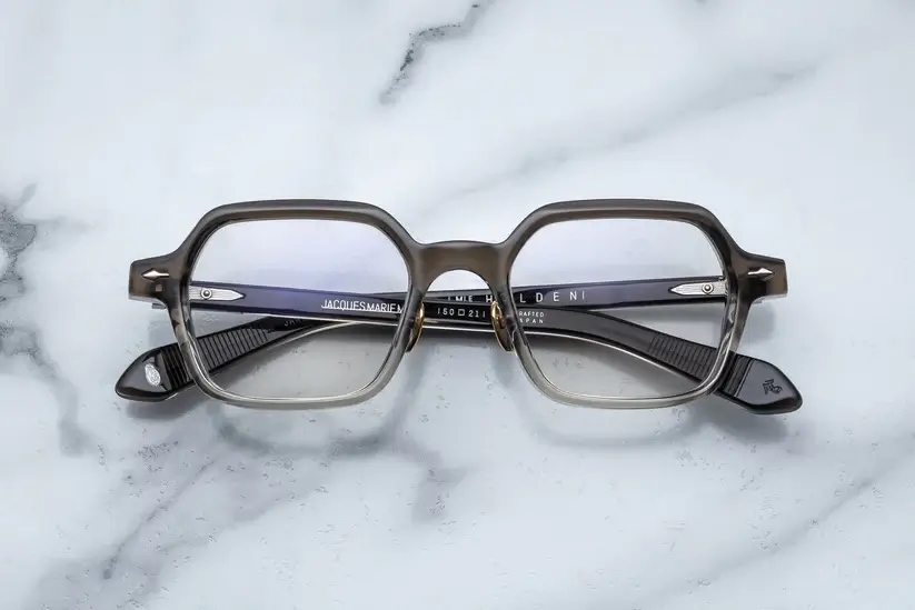 Eyeglasses with a bold square frame, displayed on a marble surface.