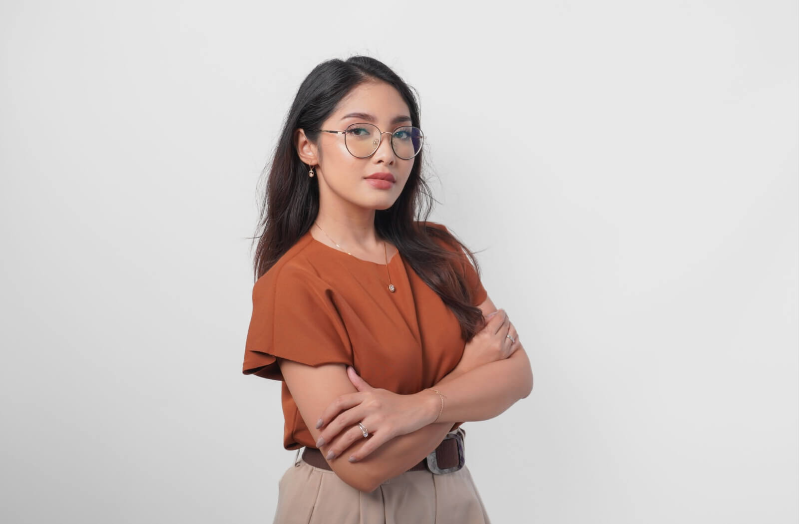 Confident young woman wearing Asian fit eyeglasses, standing with arms crossed against a plain background