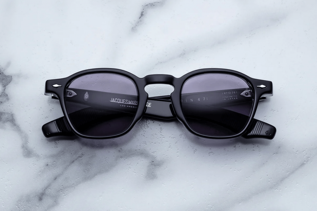 Black rectangular eyeglass frames with tinted lenses displayed on a light marble surface, showcasing a modern, minimalist designer eyewear style.