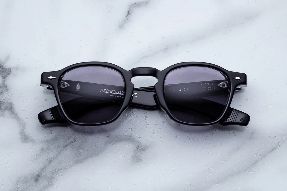 Black rectangular eyeglass frames with tinted lenses displayed on a light marble surface, showcasing a modern, minimalist designer eyewear style.