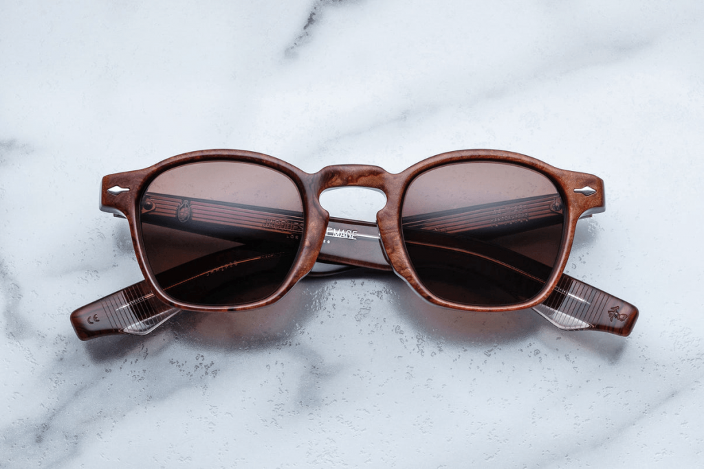 Brown rectangular eyeglass frames with tinted lenses displayed on a light marble surface, highlighting a classic, handcrafted designer eyewear aesthetic.