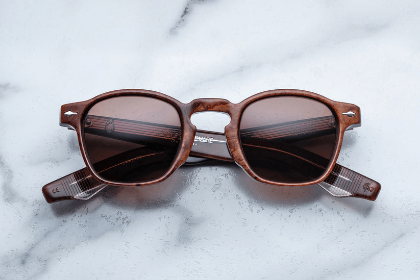 Brown-framed sunglasses with dark lenses resting on a light marble surface.