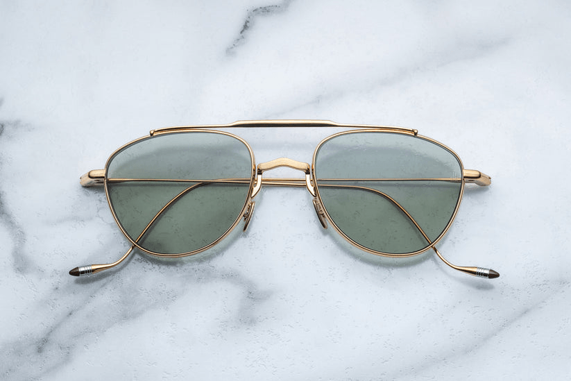 Gold metal eyeglasses with lightly tinted lenses resting on a light marble surface.