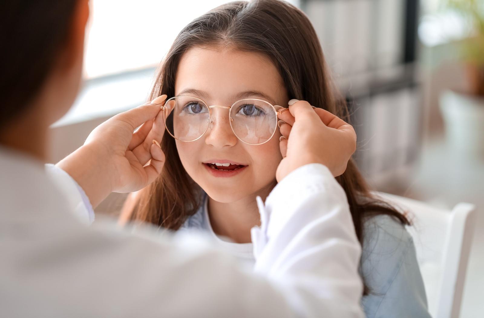 An optician putting a pair of glasses on a young patient.