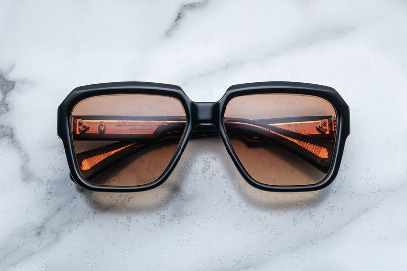 square sunglasses with matte black frames and tinted orange lenses on a marble surface.